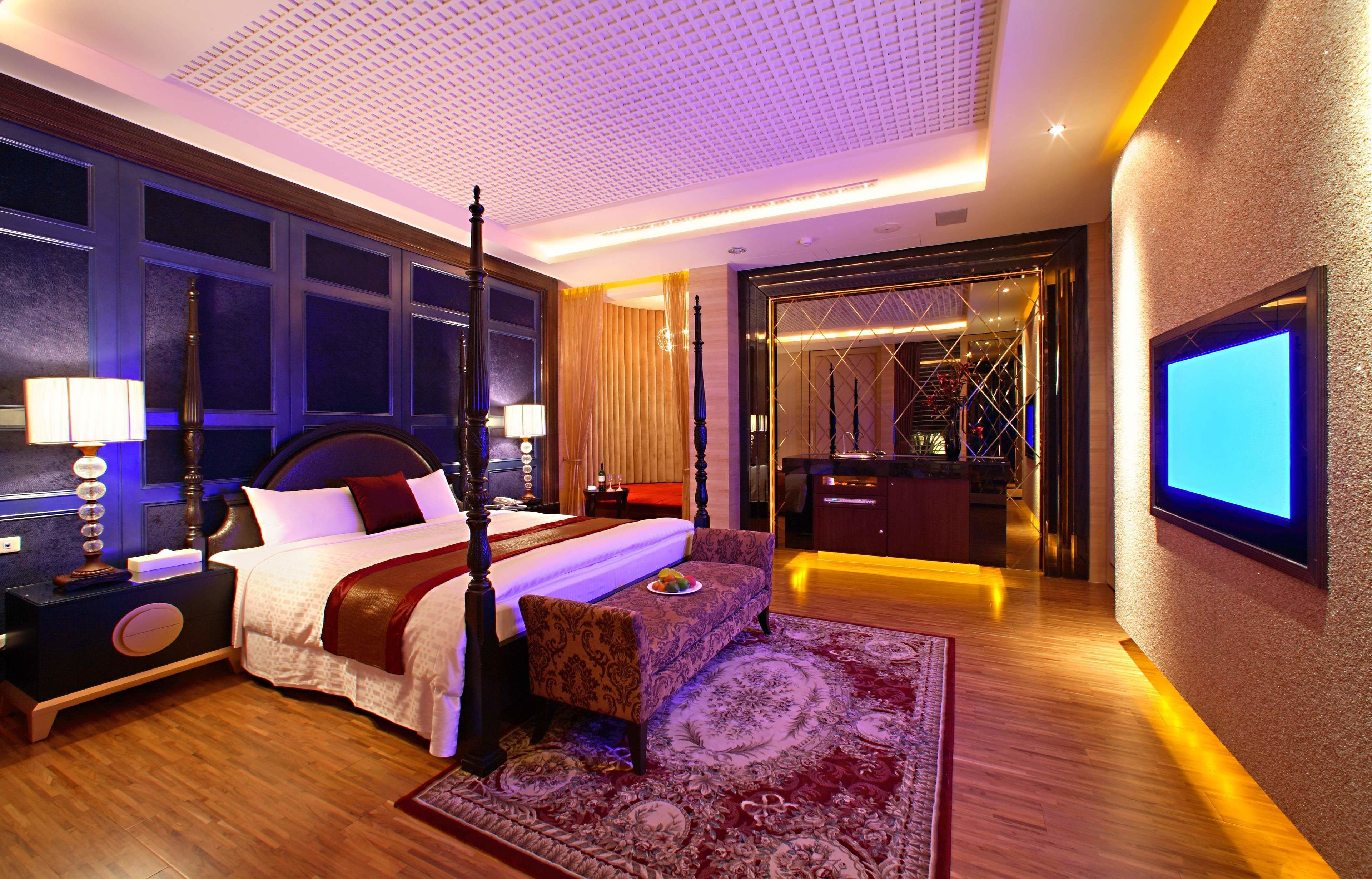 A luxurious bedroom with a large bed, a bedside table, a nightstand, a TV mounted on the wall, and a mirror.
