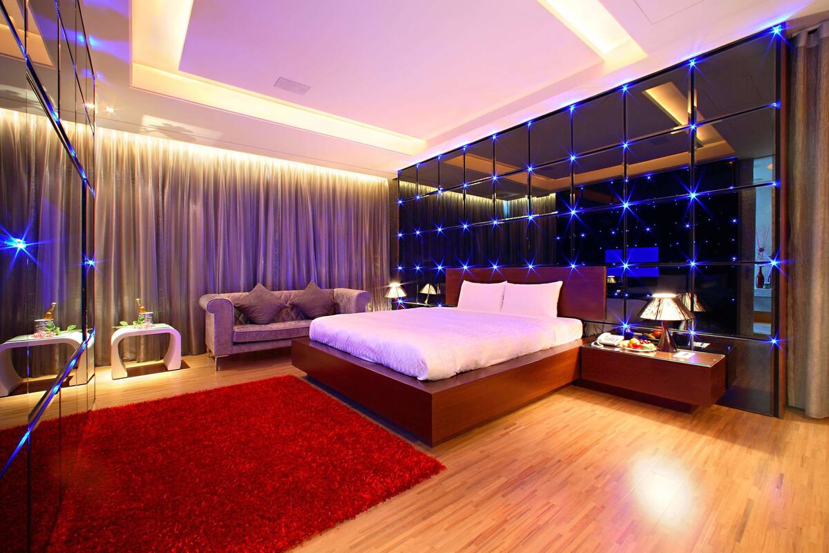 A modern bedroom with a large bed, a red rug, and a mirror wall with star lights.