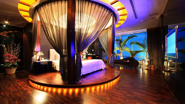A luxurious bedroom with a curved canopy bed, a round wooden platform, and a view of palm trees through large windows. - Changhua KuiKuan Boutique Motel (Changhua)