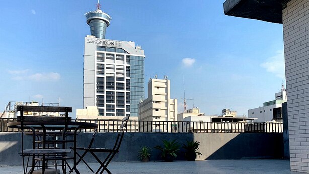 A rooftop terrace with a metal table and chairs, potted plants, and a view of a tall building with a control tower. - Backpacker 41 hostel - Taichung (Taichung)