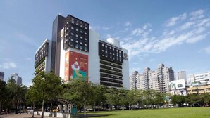 A modern high-rise building with a large advertisement on its side, surrounded by a park with trees and a clear sky. - Backpacker 41 hostel - Taichung (Taichung)