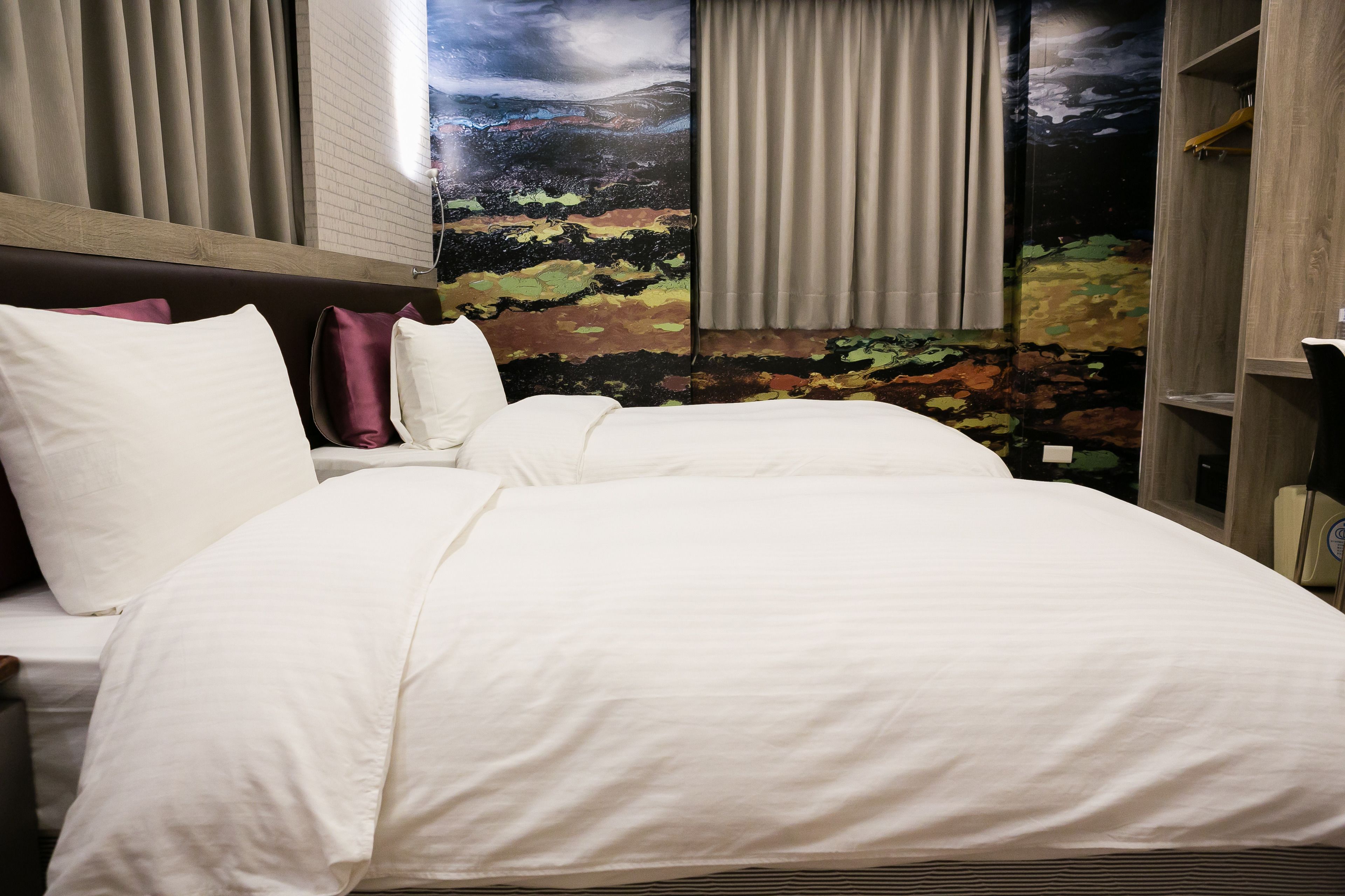 A hotel room with a large bed, a headboard, a wardrobe, and a mural on the wall.