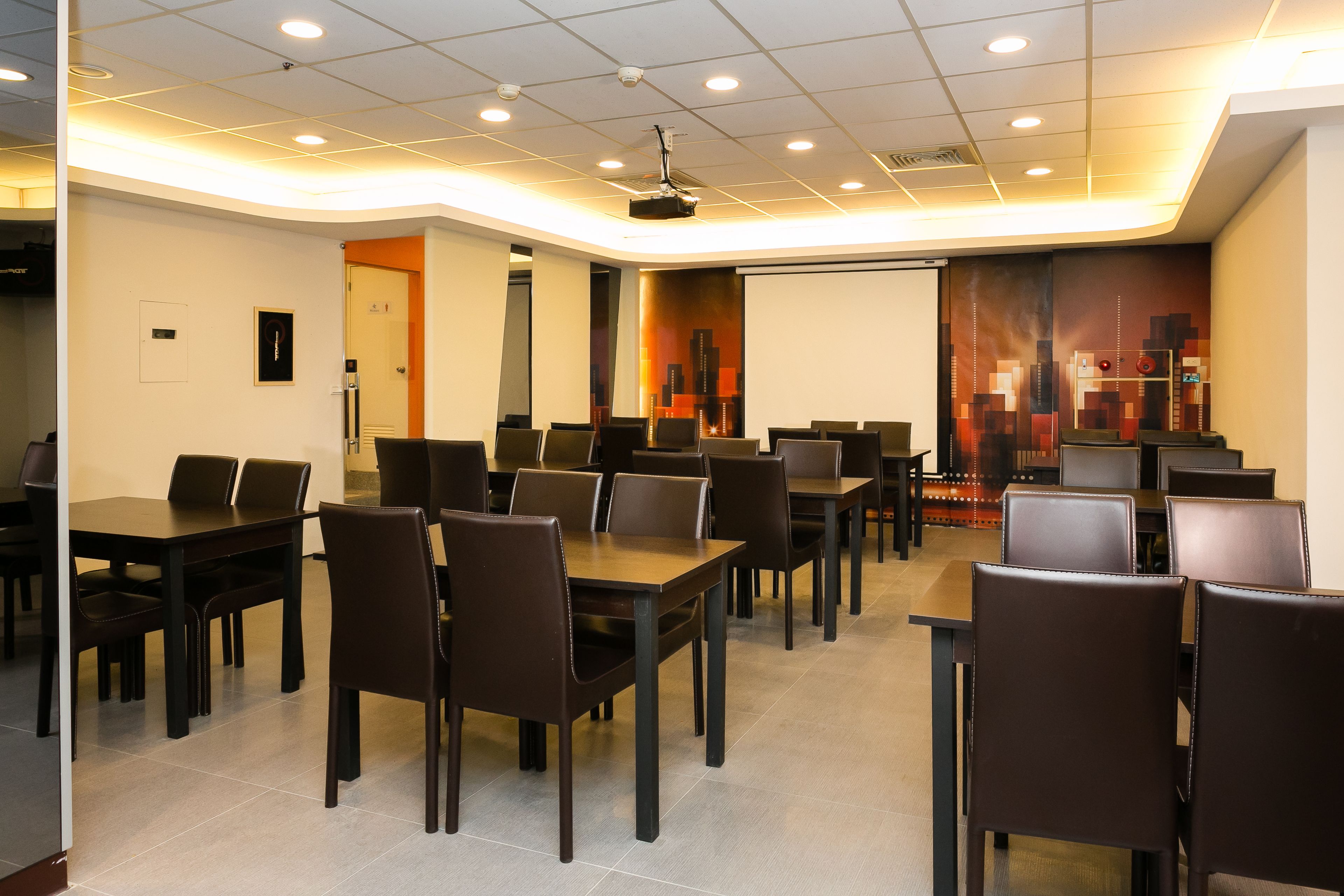A conference room with multiple tables and chairs, a projector screen, and a cityscape mural on the wall.