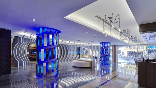 A modern hotel lobby with a reception desk, blue illuminated columns, and a large window offering a view of the street. - Yuhao Hotel Hsinchu (Hsinchu)