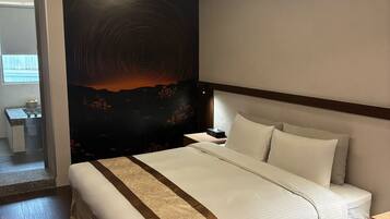A modern hotel room with a large bed, a nightstand, a wall-mounted TV, and a view of the outdoors.