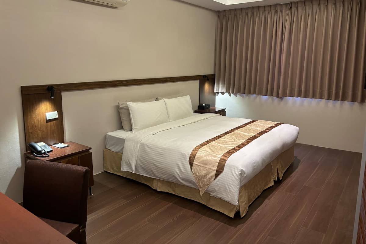 A hotel room with a bed, bedside table, lamp, and a phone.