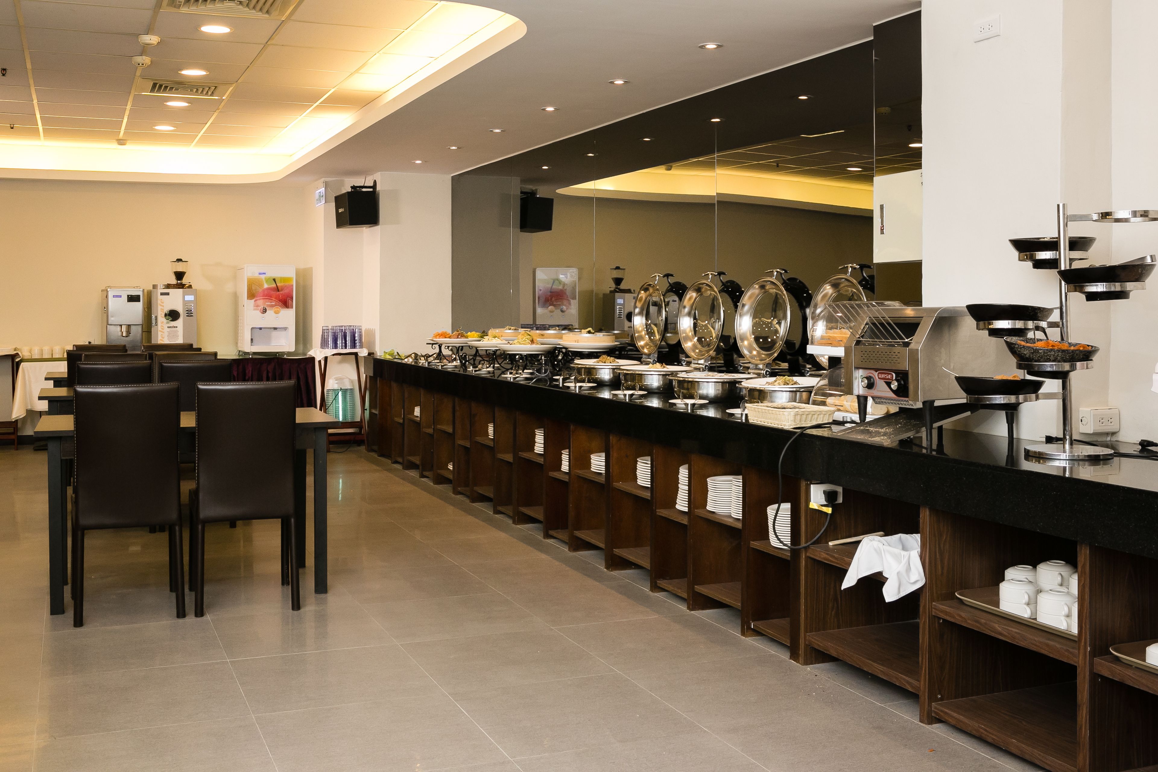 Een buffetopstelling met verschillende bedieningspunten, een koffieapparaat en een zithoek met stoelen.