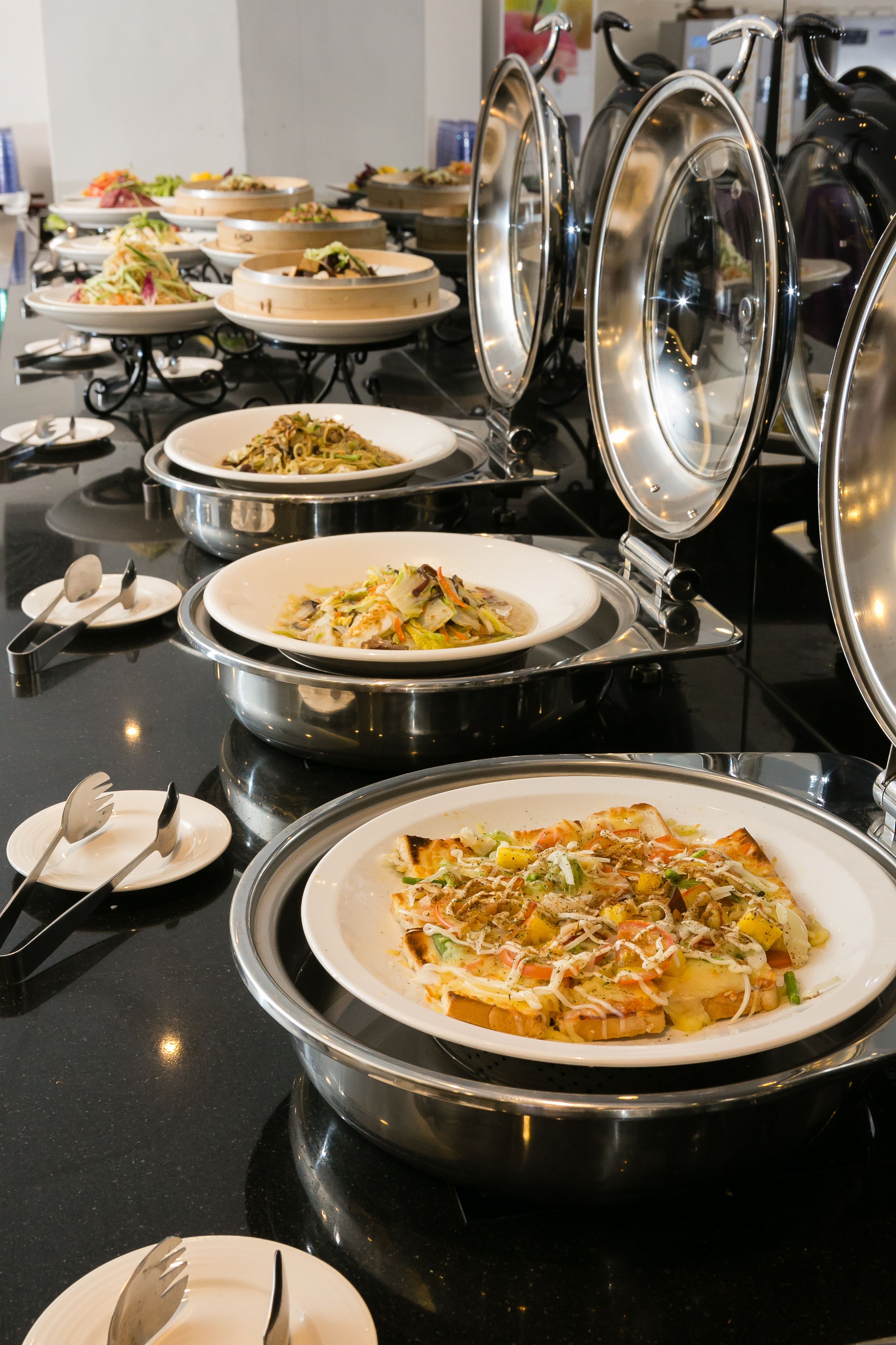 Servicio de comidas tipo buffet con diversos platos y utensilios sobre una encimera negra.