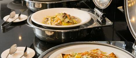 Servicio de comidas tipo buffet con diversos platos y utensilios sobre una encimera negra.