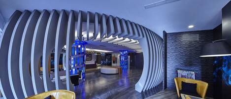 A modern lobby with a curved wall design, a reception desk, seating area, and a wall with a blue light feature.