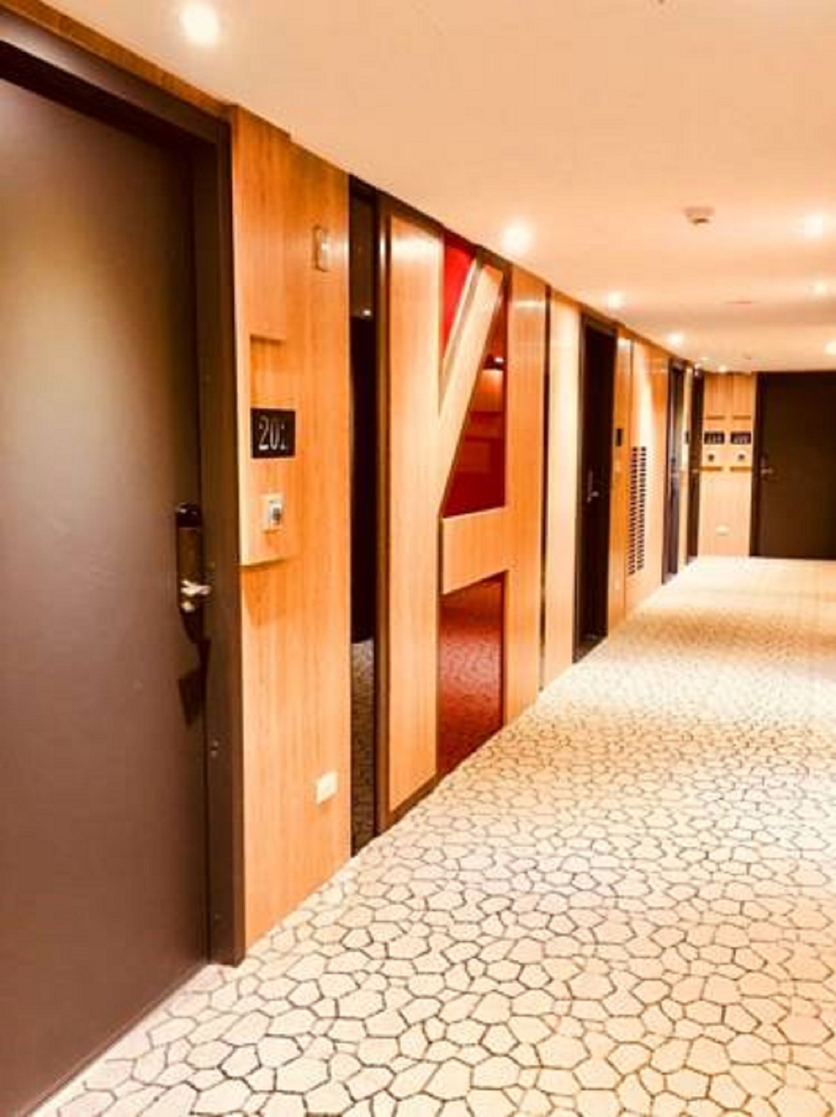 A hotel corridor with wooden doors, a tiled floor, and a staircase.