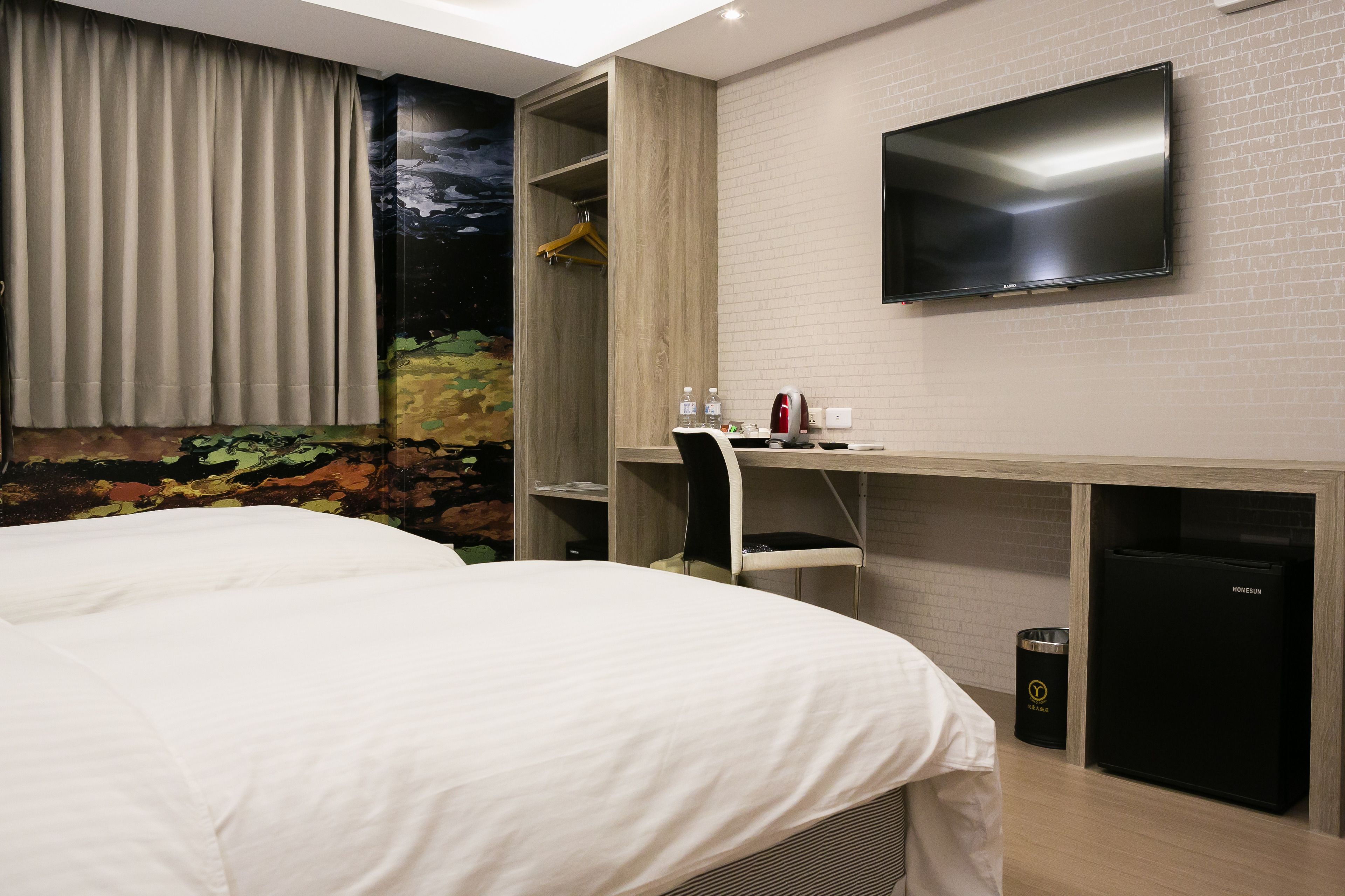 A hotel room with a bed, a desk with a chair, a television, and a minibar.