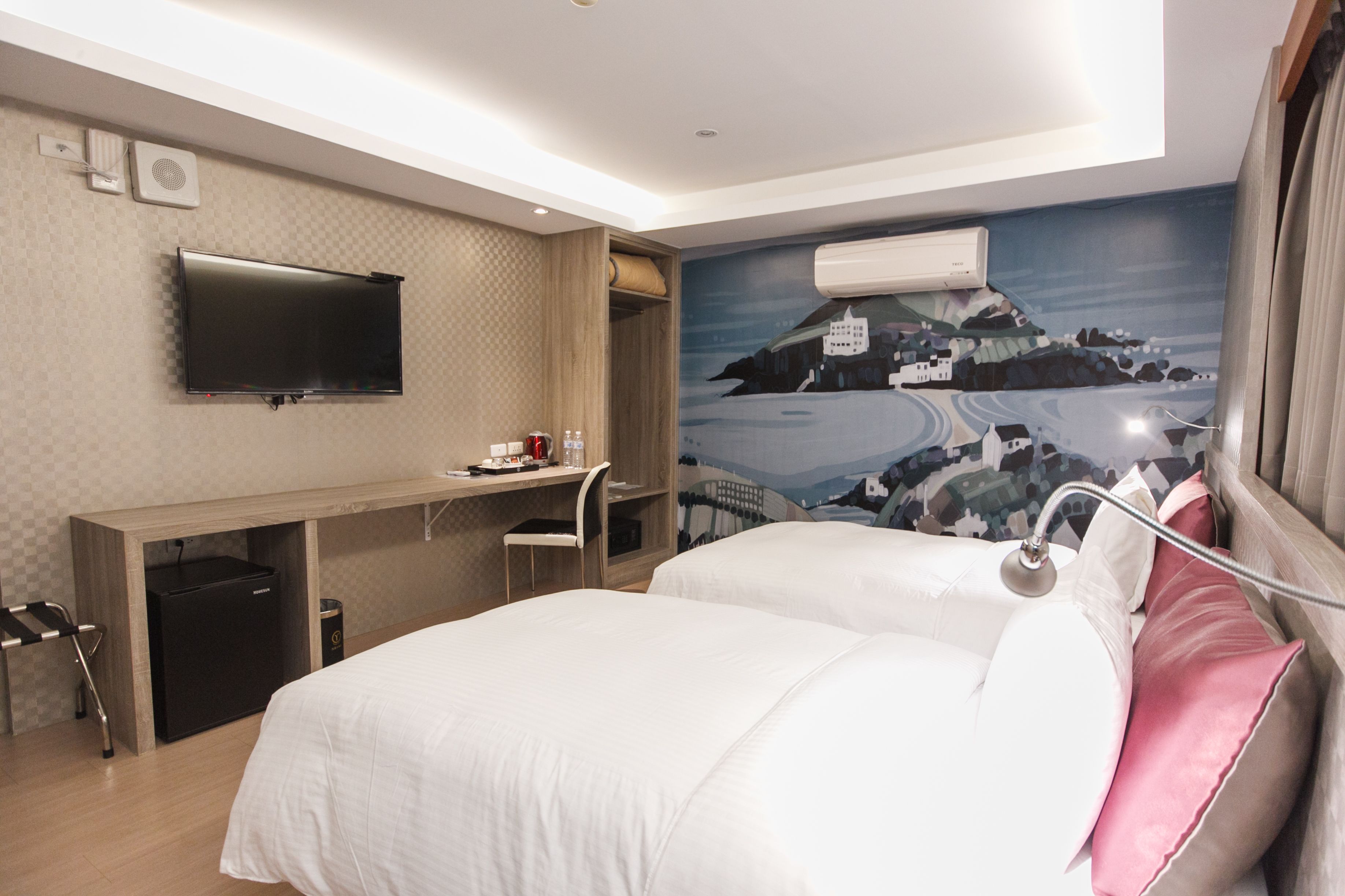 Een hotelkamer met een bed, een bureau, een stoel, een televisie en een muurschildering.