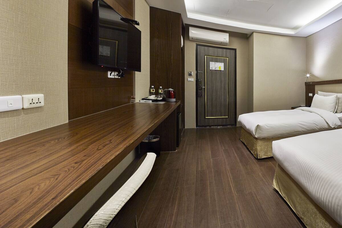 A hotel room with two beds, a wooden desk, a flat-screen TV, and a minibar.