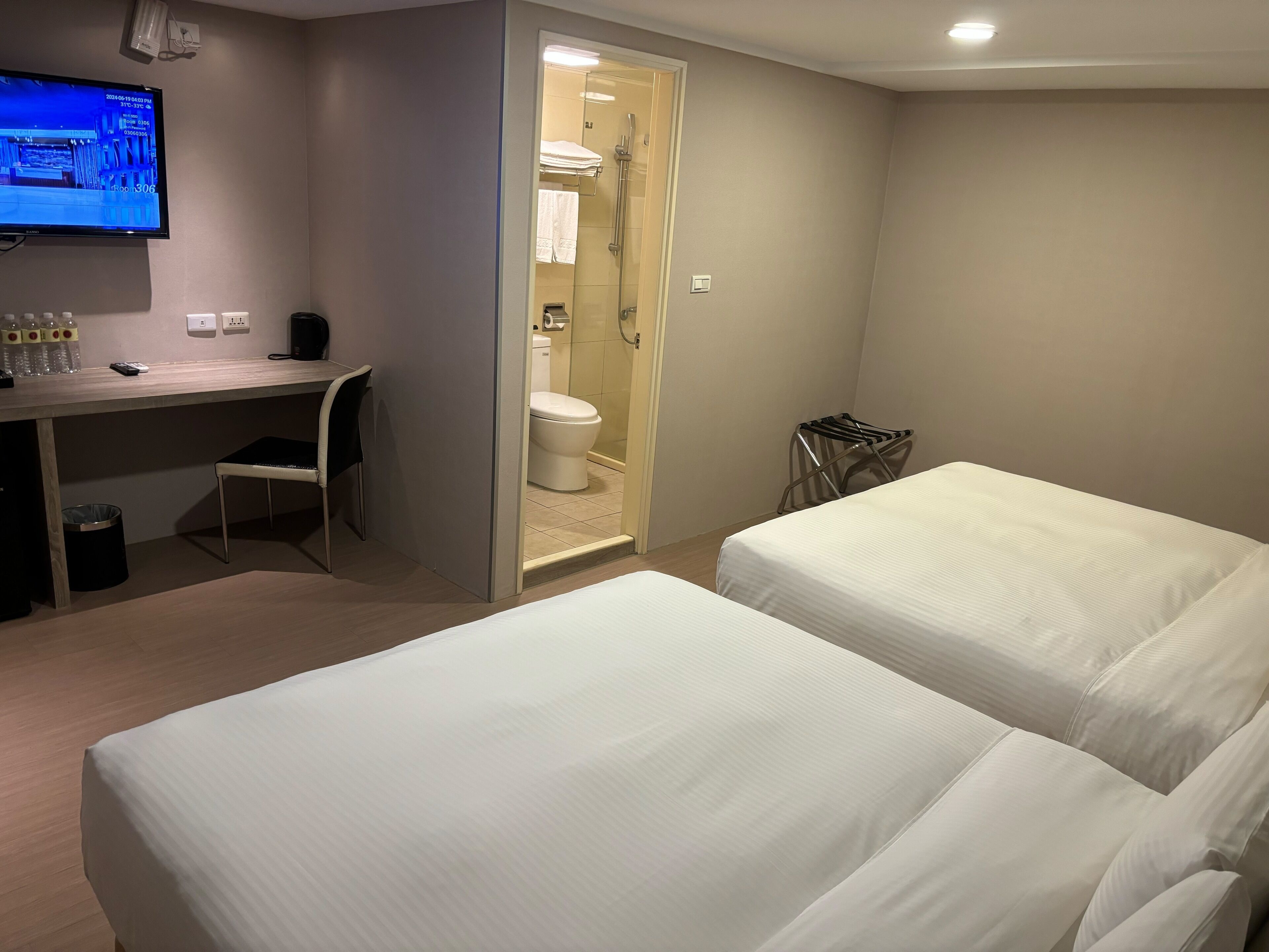 Une chambre d’hôtel avec deux lits, un bureau avec une chaise, une télévision et un espace douche.