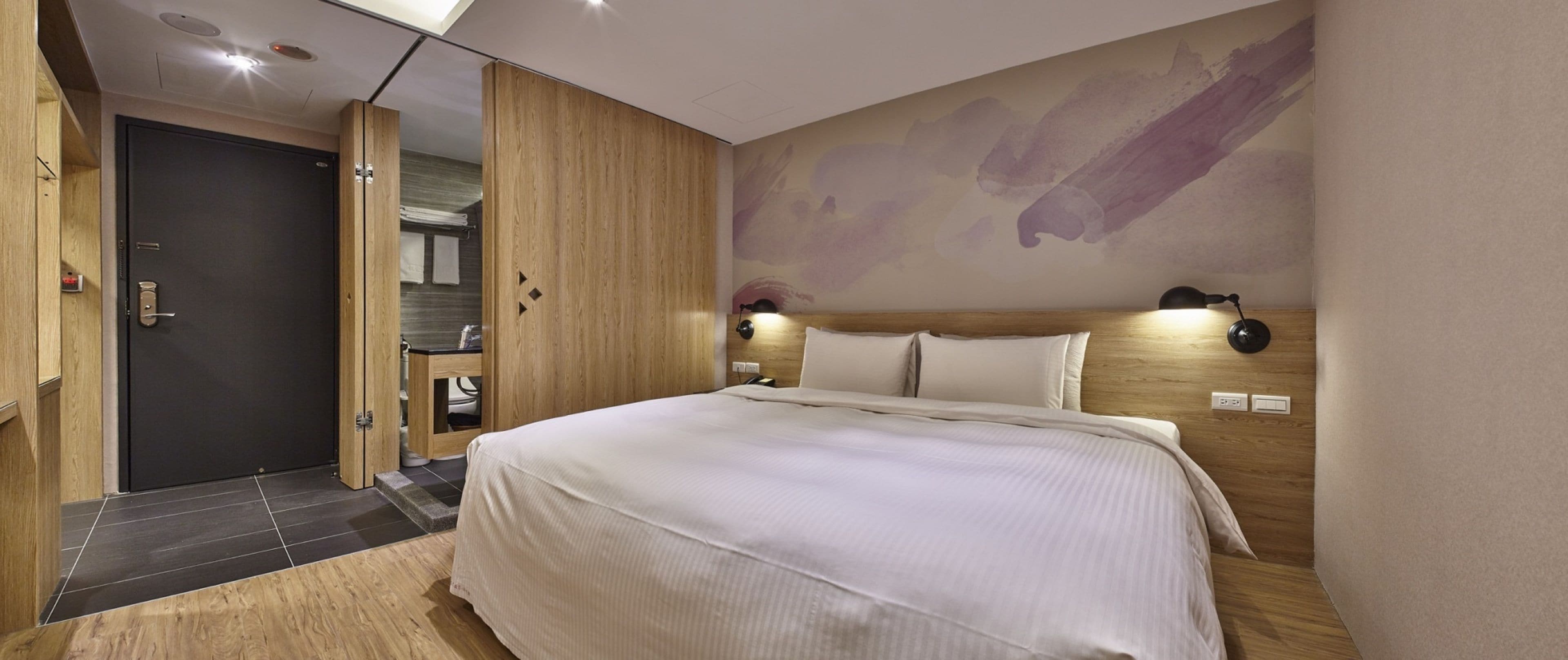 A modern bedroom with a large bed, wooden wardrobe, and a wall-mounted lamp.