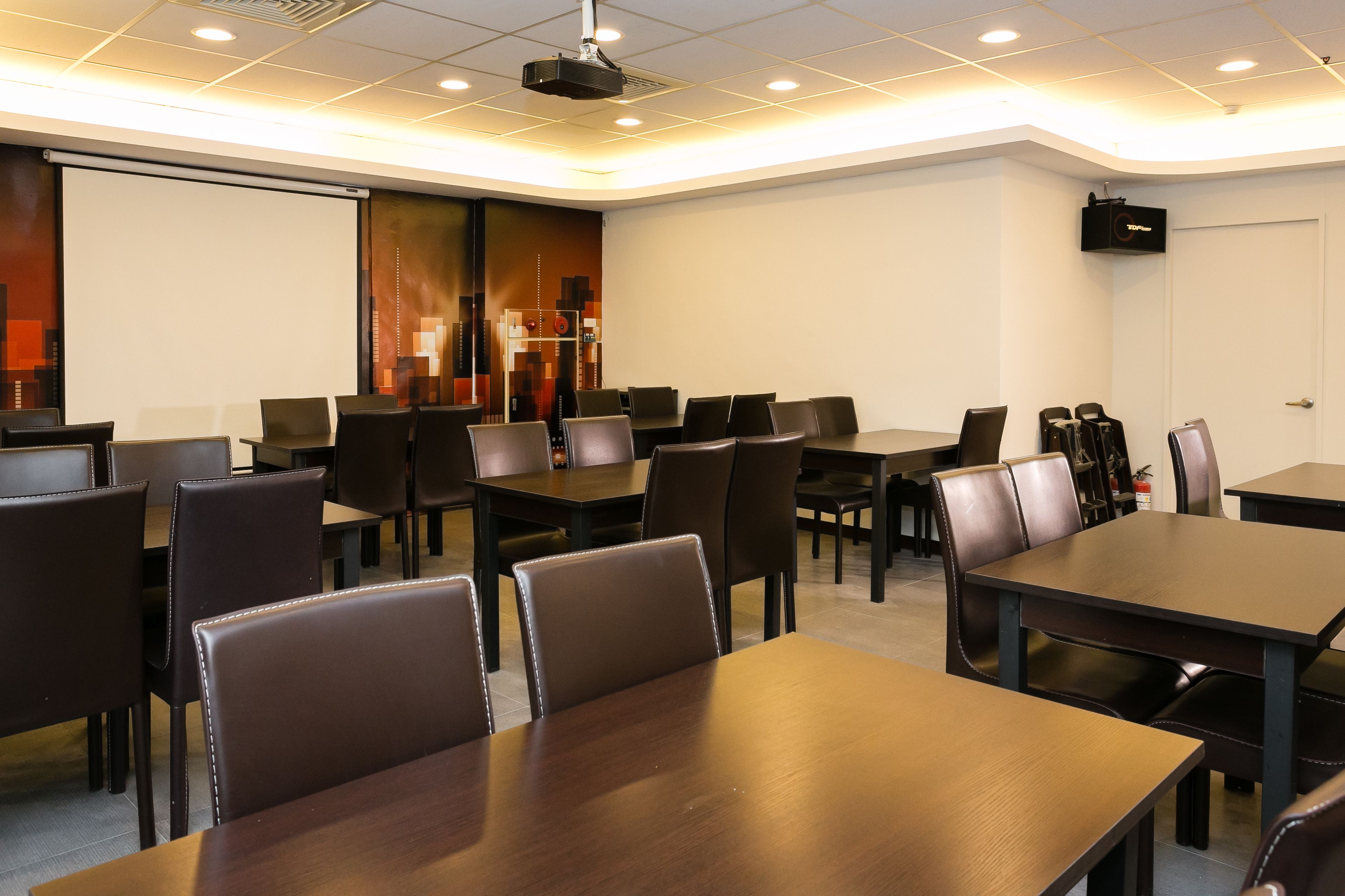 Una sala de conferencias con varias mesas y sillas, un proyector y una pantalla.