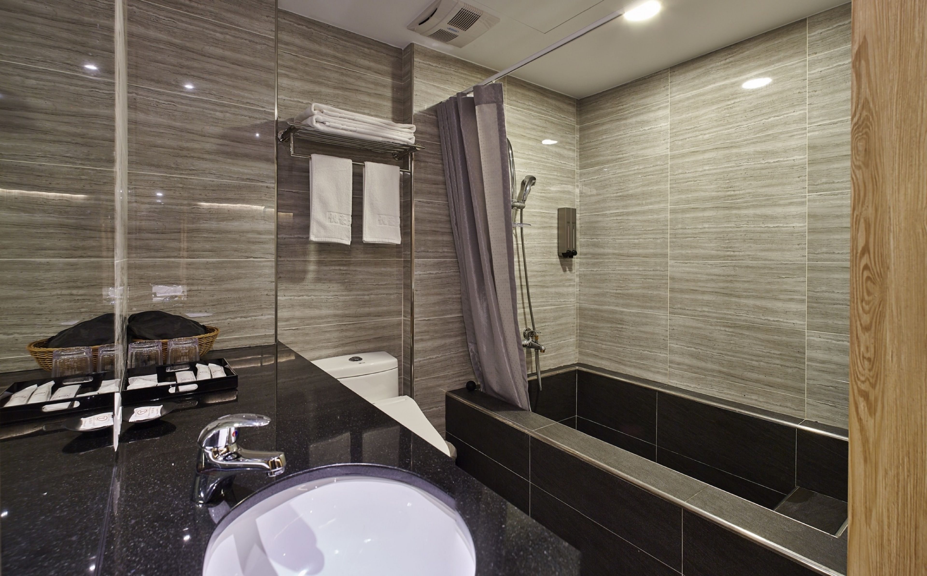 Un baño moderno con encimera negra, lavamanos, ducha con puerta de vidrio y toallero con toallas dobladas.
