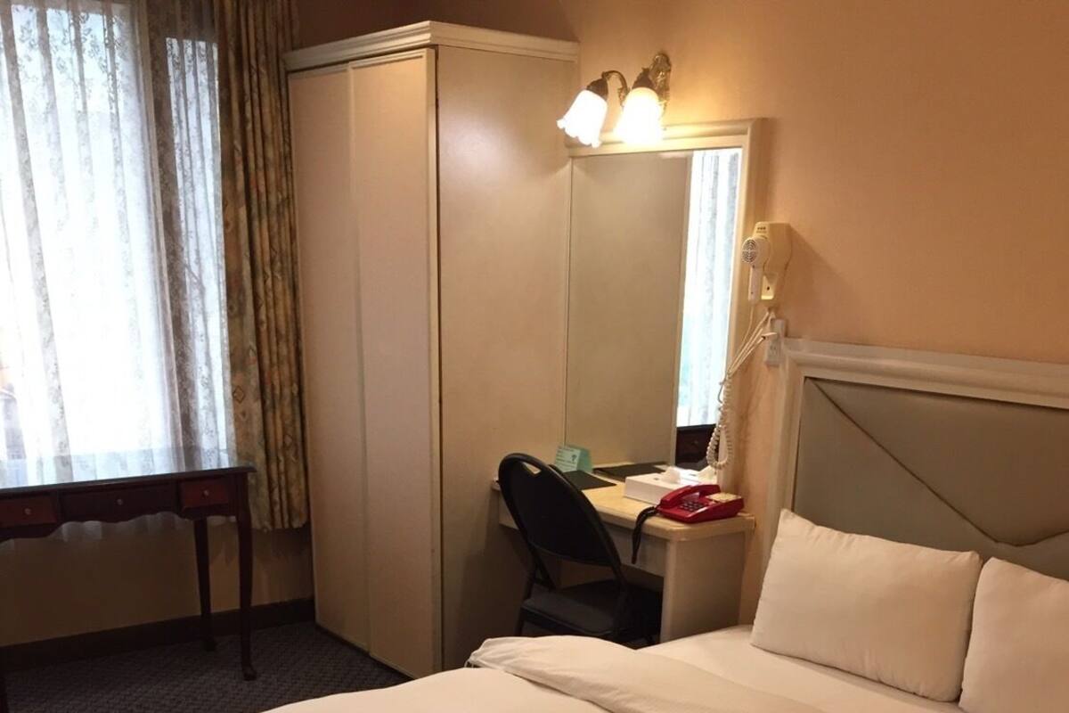 Une chambre d’hôtel comprenant un lit, un bureau, une chaise, une armoire et un miroir.