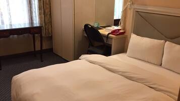 A hotel room with a bed, a desk, a chair, a wardrobe, and a mirror.