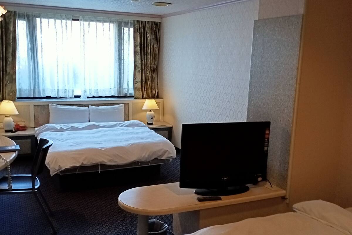 Une chambre d’hôtel avec deux lits, un bureau, une télévision et une fenêtre avec des rideaux.