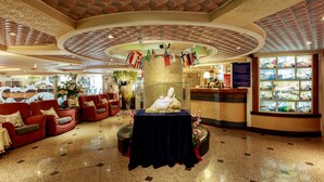 A lobby with a central statue, red sofas, a table with a dark cloth, and a display of flags.