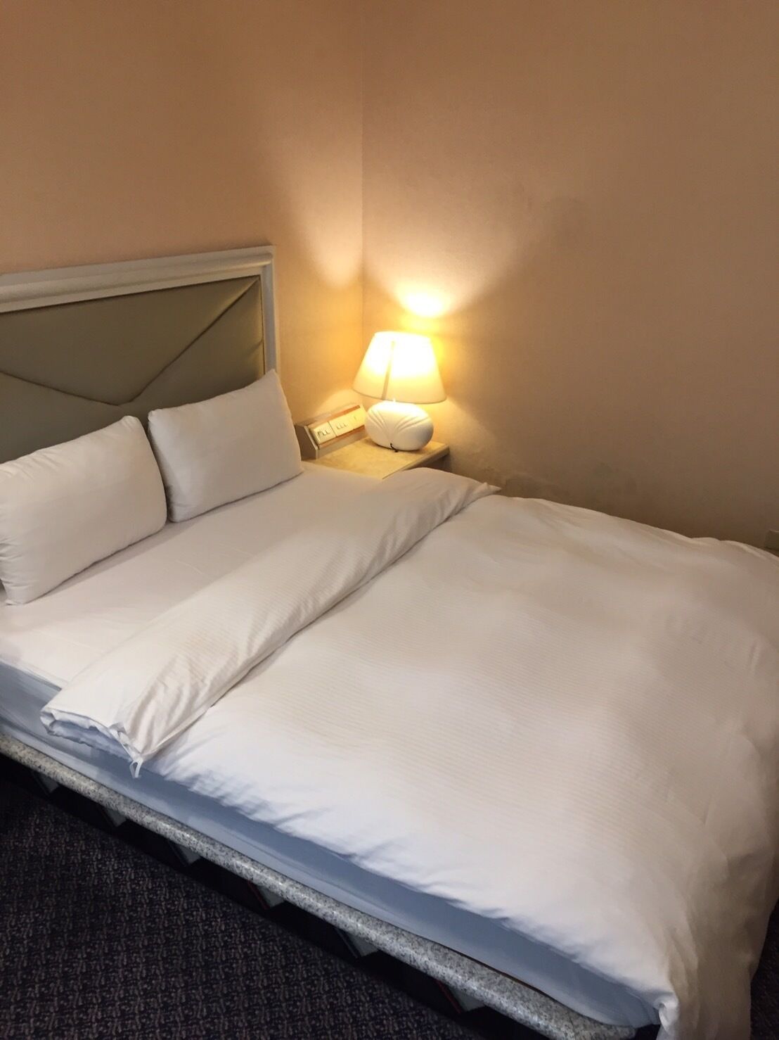 A neatly made bed with white linens and a bedside lamp.