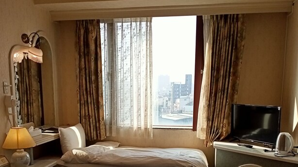 A hotel room with two beds, a desk with a television, a lamp, and a view of the city through large windows.