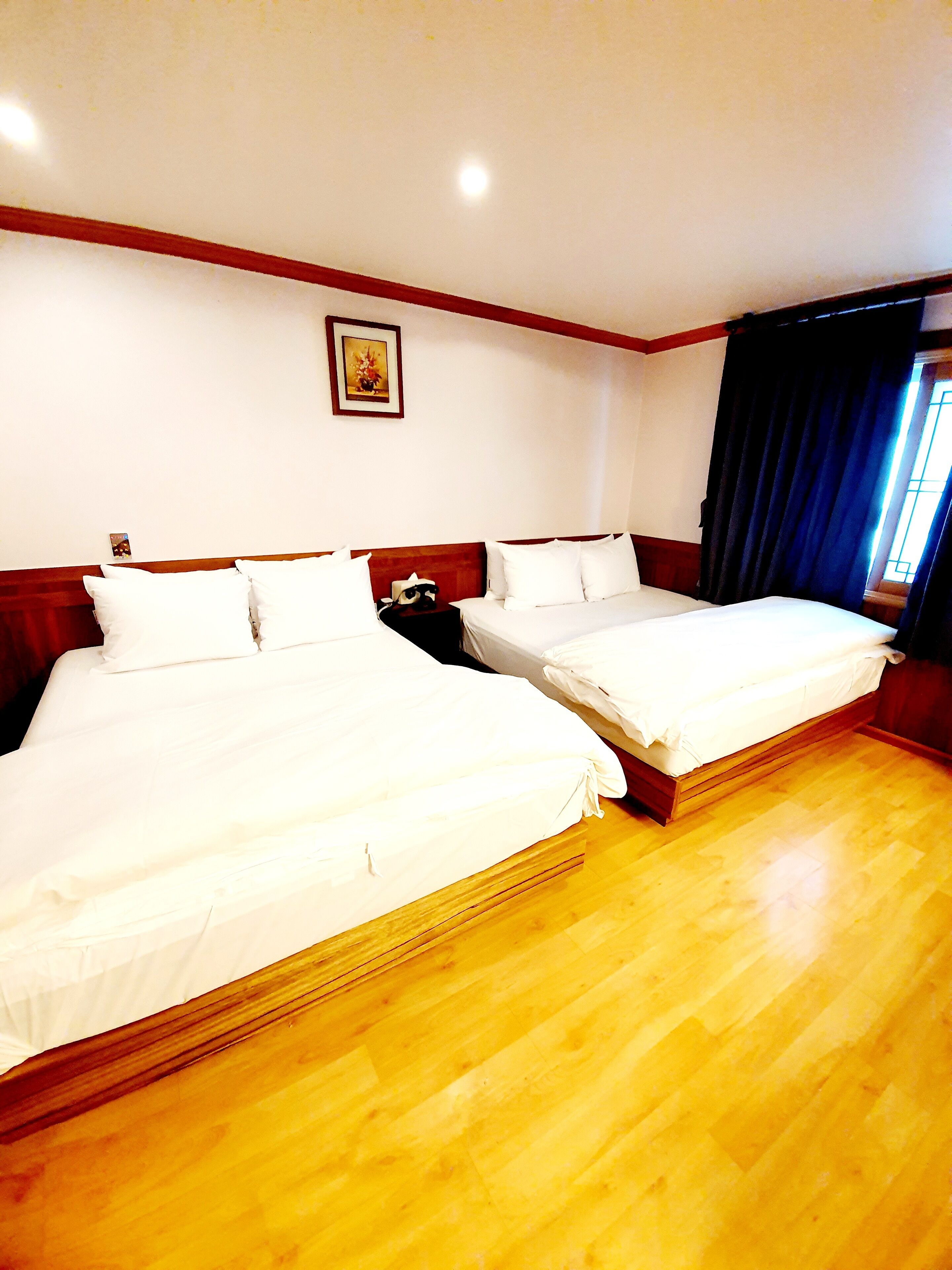 Habitación de hotel con dos camas, suelo de madera, una mesita de noche y un cuadro en la pared.