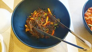 A bowl of stir-fried vegetables on a table with a woven placemat underneath.