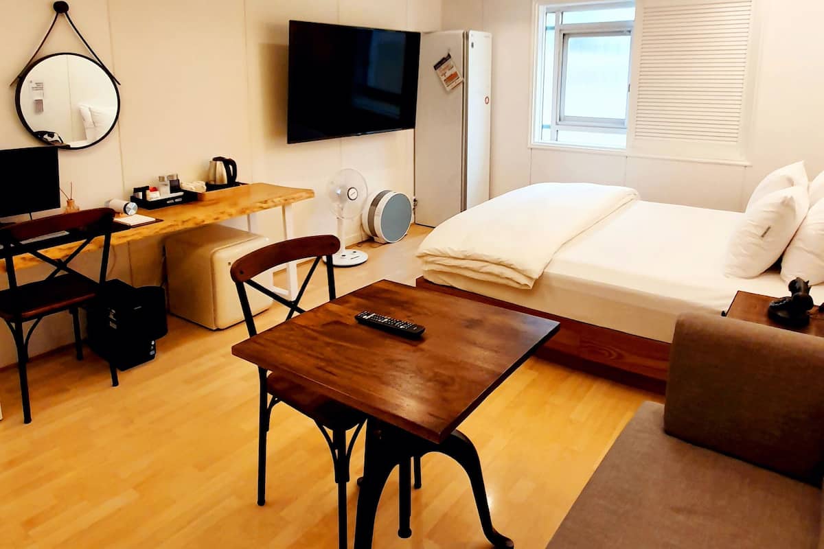 Una habitación moderna y luminosa con suelo de madera, una cama, un sofá, un escritorio con silla, un televisor y una lámpara de techo.
