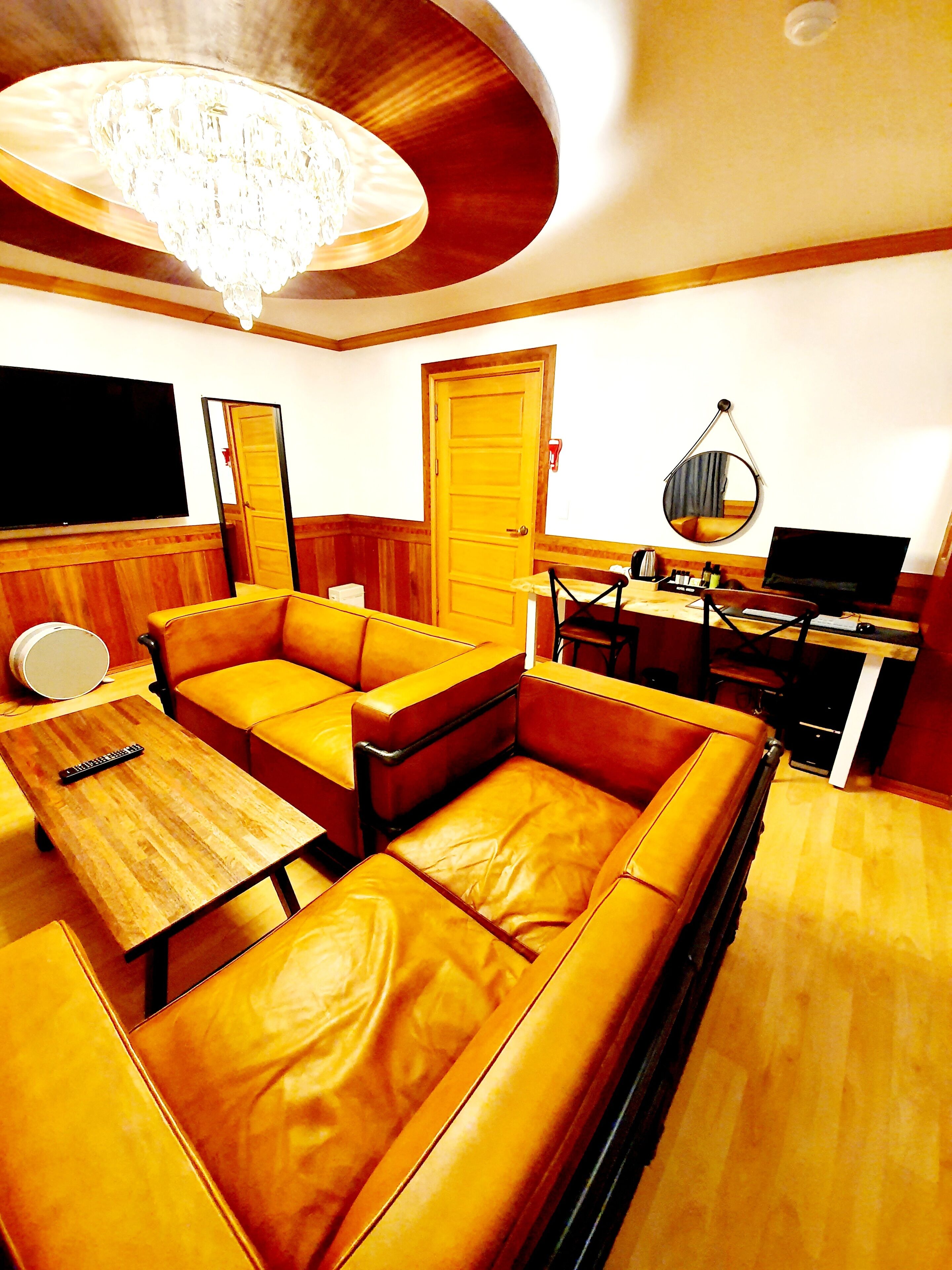 A modern living room with a large L-shaped sofa, a wooden coffee table, a TV, a desk with a computer, and a chandelier.