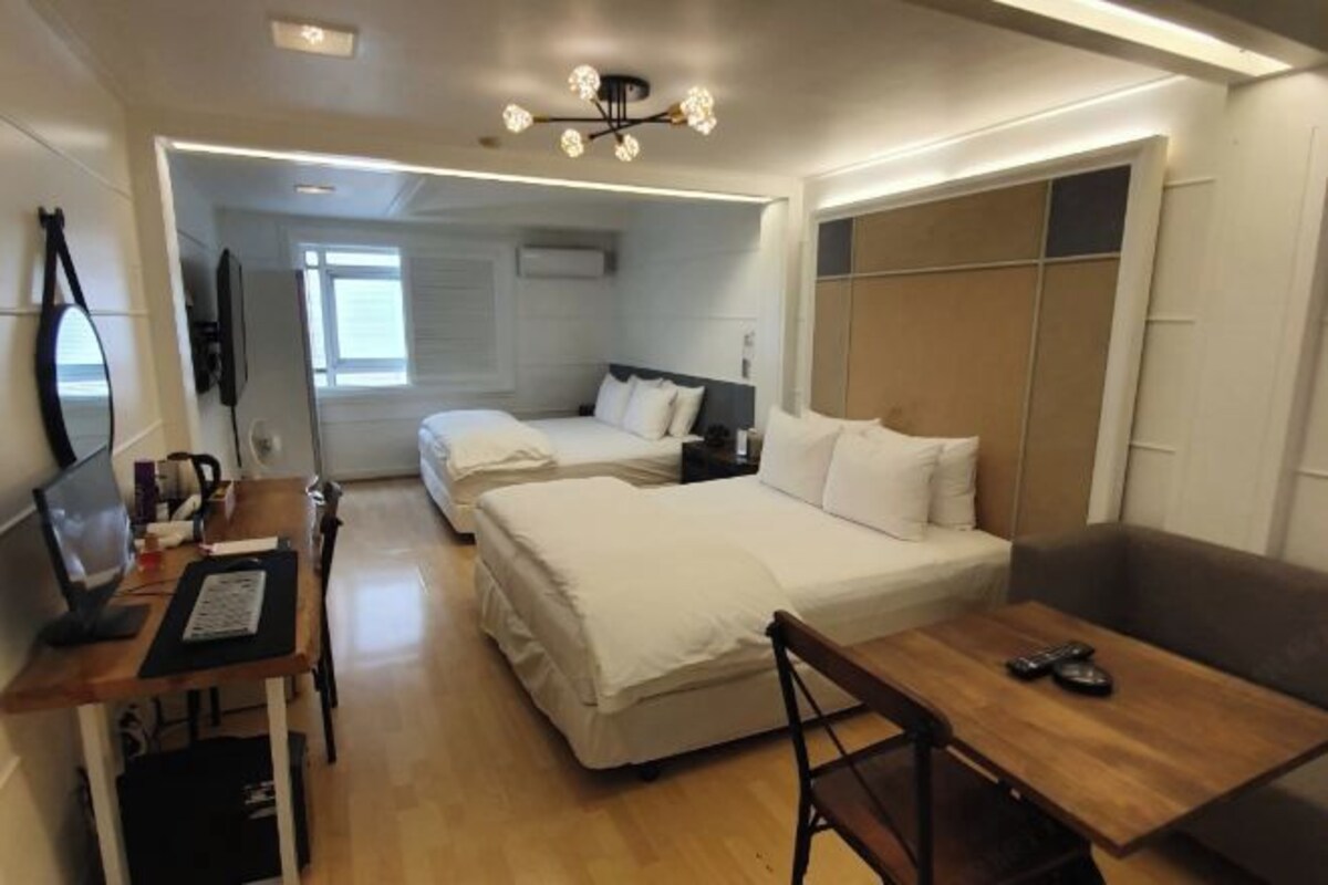 A hotel room with two beds, a desk, and a chair. There is a TV on the desk and a window in the room.