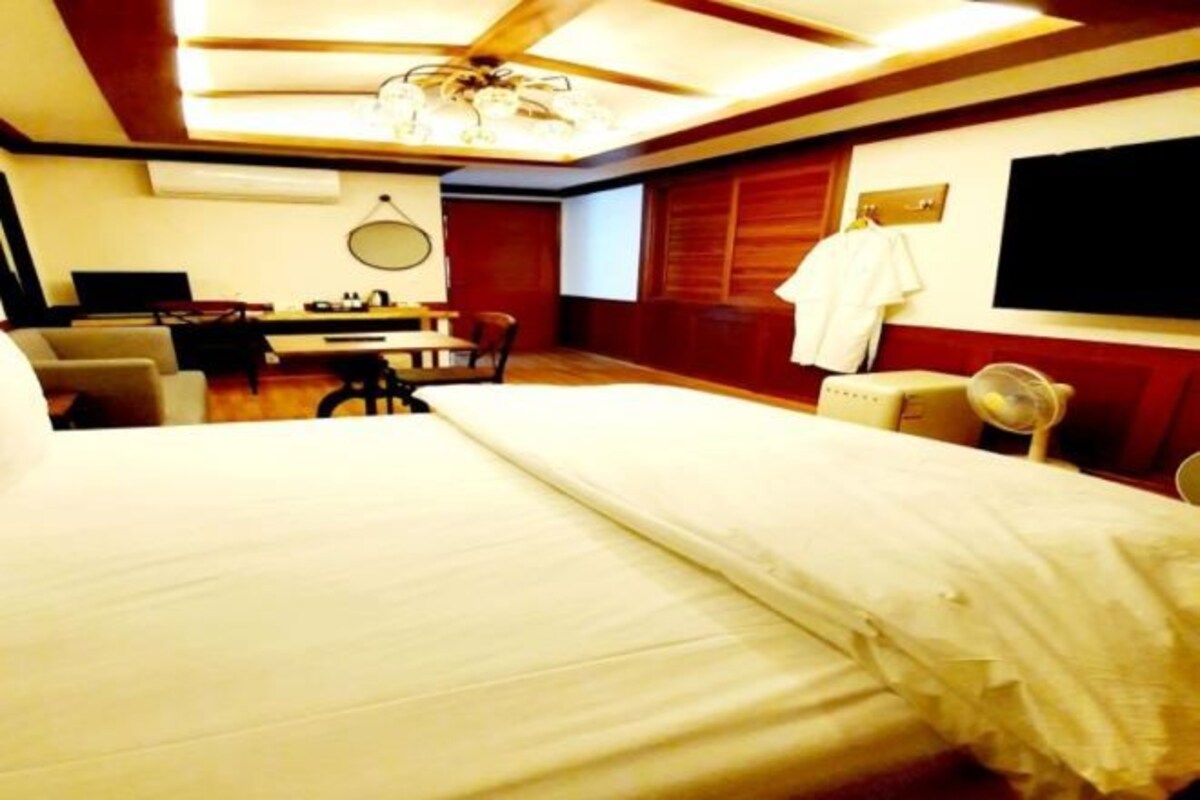 A hotel room with a large bed, a desk with a chair, a TV mounted on the wall, and a ceiling fan.