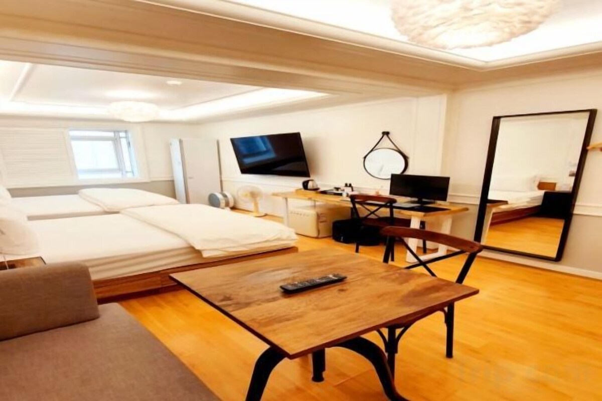 A hotel room with a bed, a desk with a computer, a TV, and a large mirror.