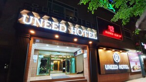 The exterior of the Uneed Hotel with a well-lit entrance, a visible staircase leading to the entrance, and a sign indicating a business club nearby.