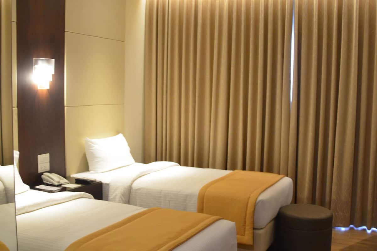 A hotel room with two beds, a bedside table with a phone, a mirror, and a large window with curtains.