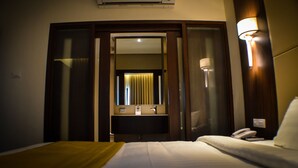 Habitación de hotel con cama, mesita de noche, espejo, teléfono en la pared y lámpara de pared.