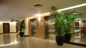 Un vestíbulo con piso pulido, dos ascensores y plantas en macetas.