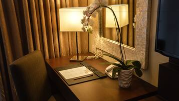 Escritorio de habitación de hotel con una lámpara, un teléfono, un bloc de notas, un bolígrafo y una planta en maceta.