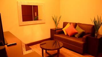 A living room with a brown sofa, a glass coffee table, a remote control, and two potted plants.