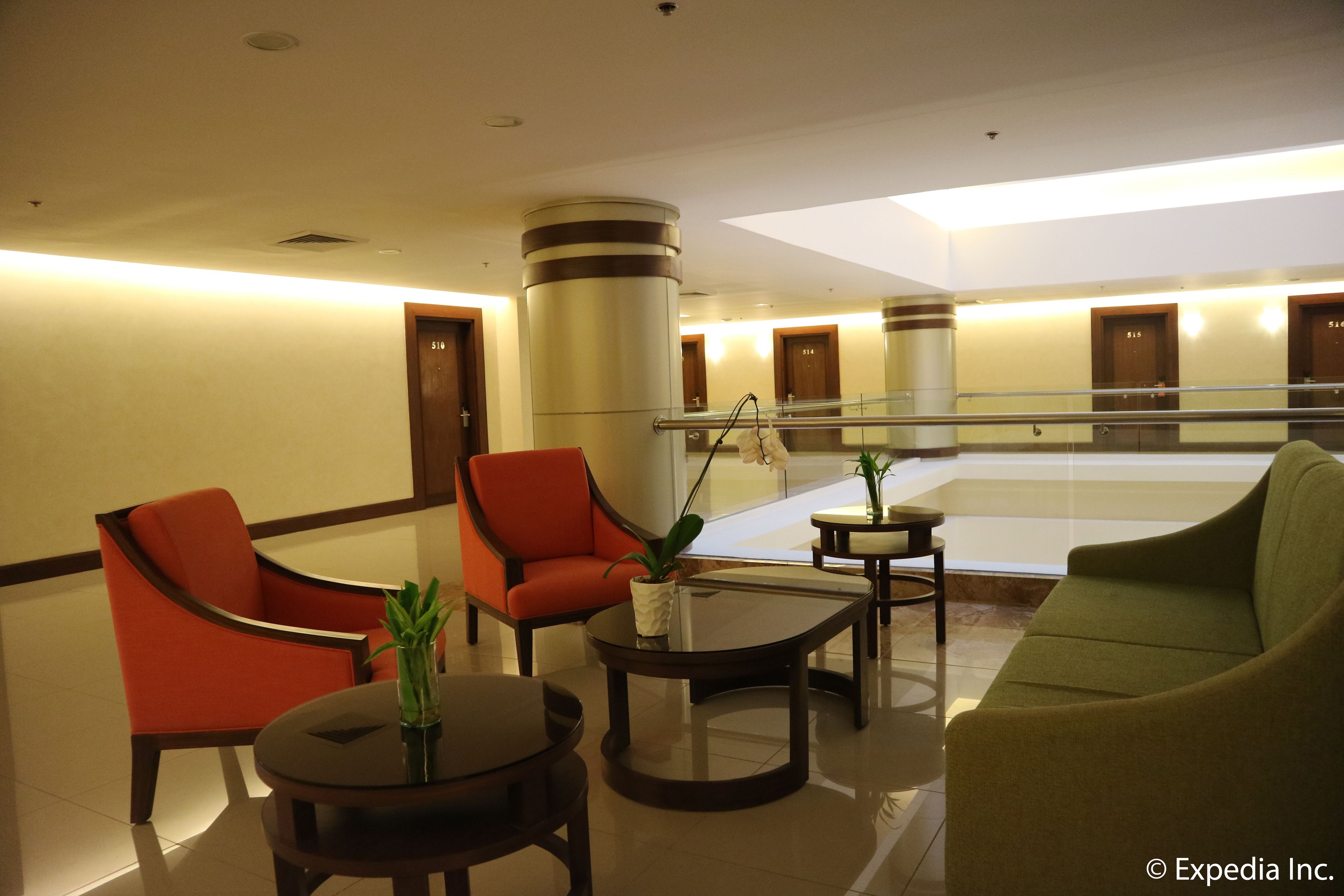 A lobby with a glass partition, red and green chairs, a round table with a plant, and a large pillar.