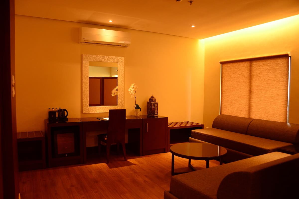 A living room with a sofa, a coffee table, a desk with a chair, and a small table with a vase of flowers.