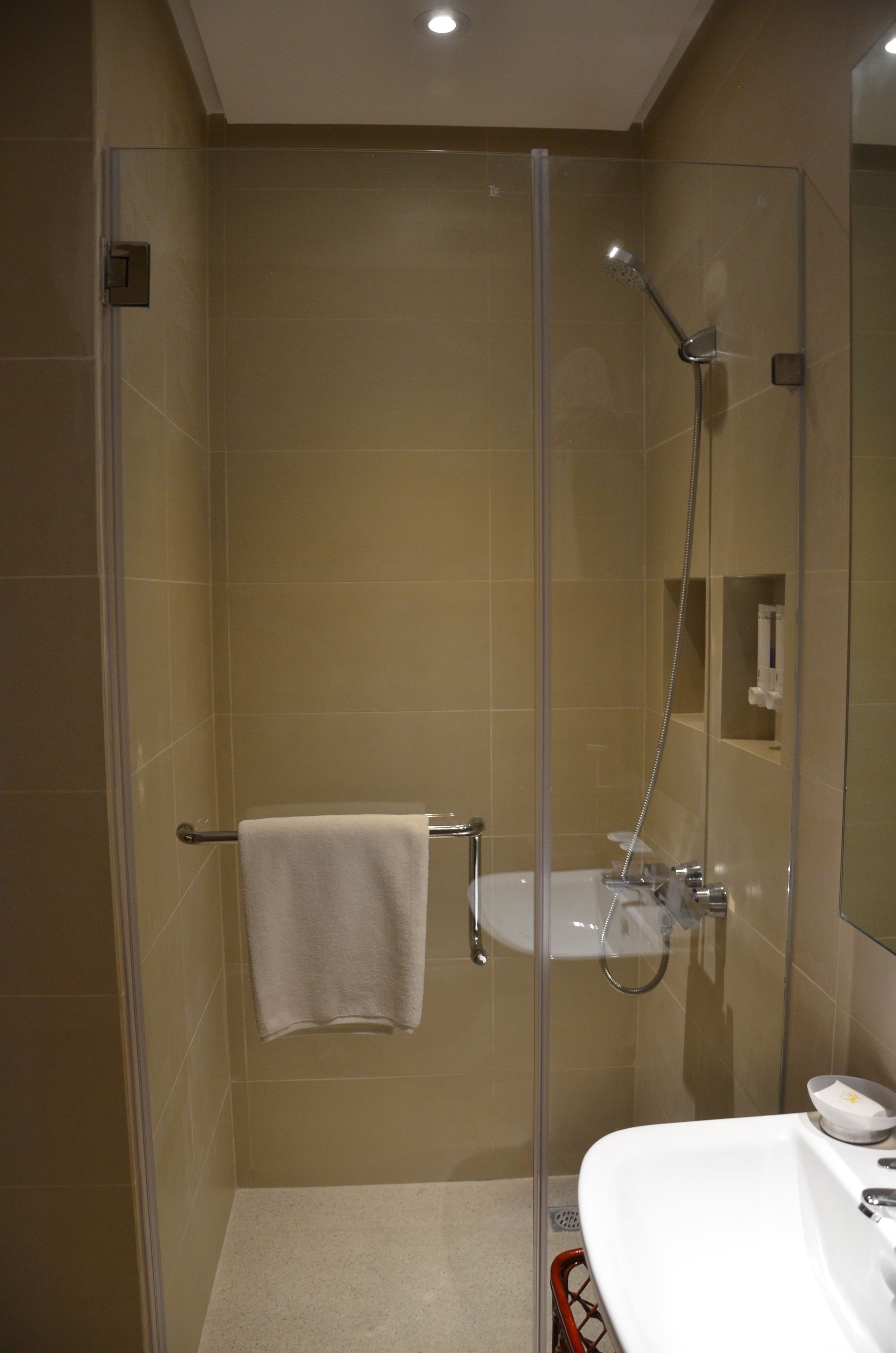 Een moderne badkamer met een douchecabine van glas, een wit wastafeltje en een handdoekrek.
