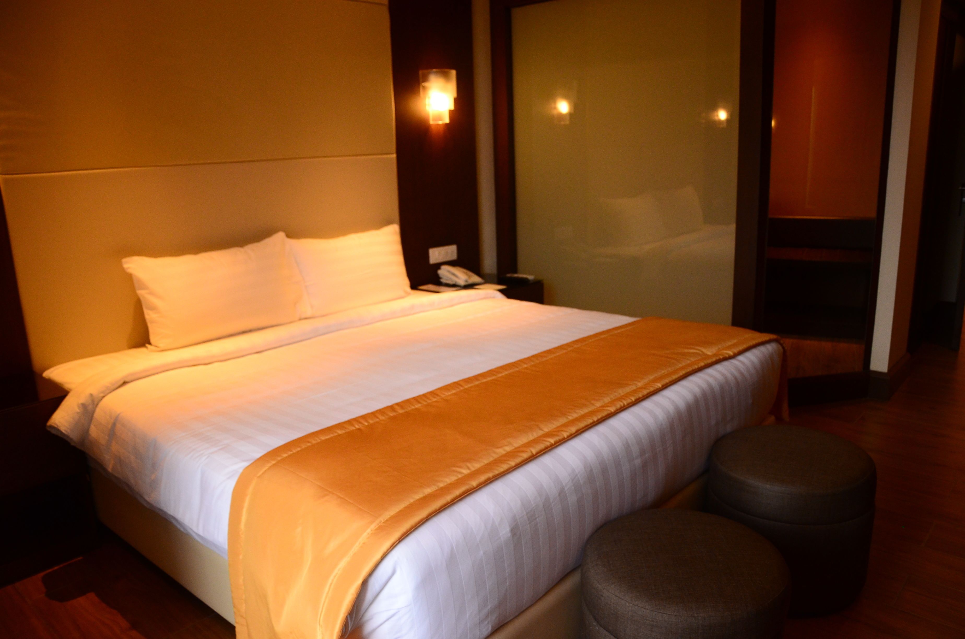 Una habitación de hotel con una cama grande, una mesita de noche, un teléfono y un separador de vidrio.