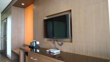 A modern hotel room with a wooden vanity, a flat-screen TV mounted on the wall, and a small table with a kettle and a book.