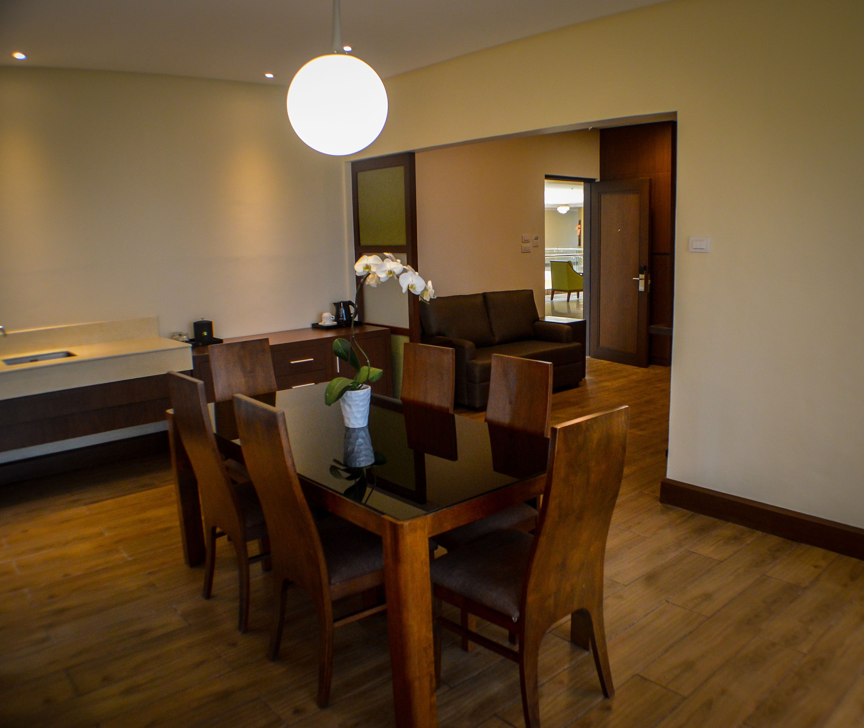 Un coin repas avec une table en bois, des chaises, un vase orné d’une orchidée et un luminaire suspendu lumineux.
