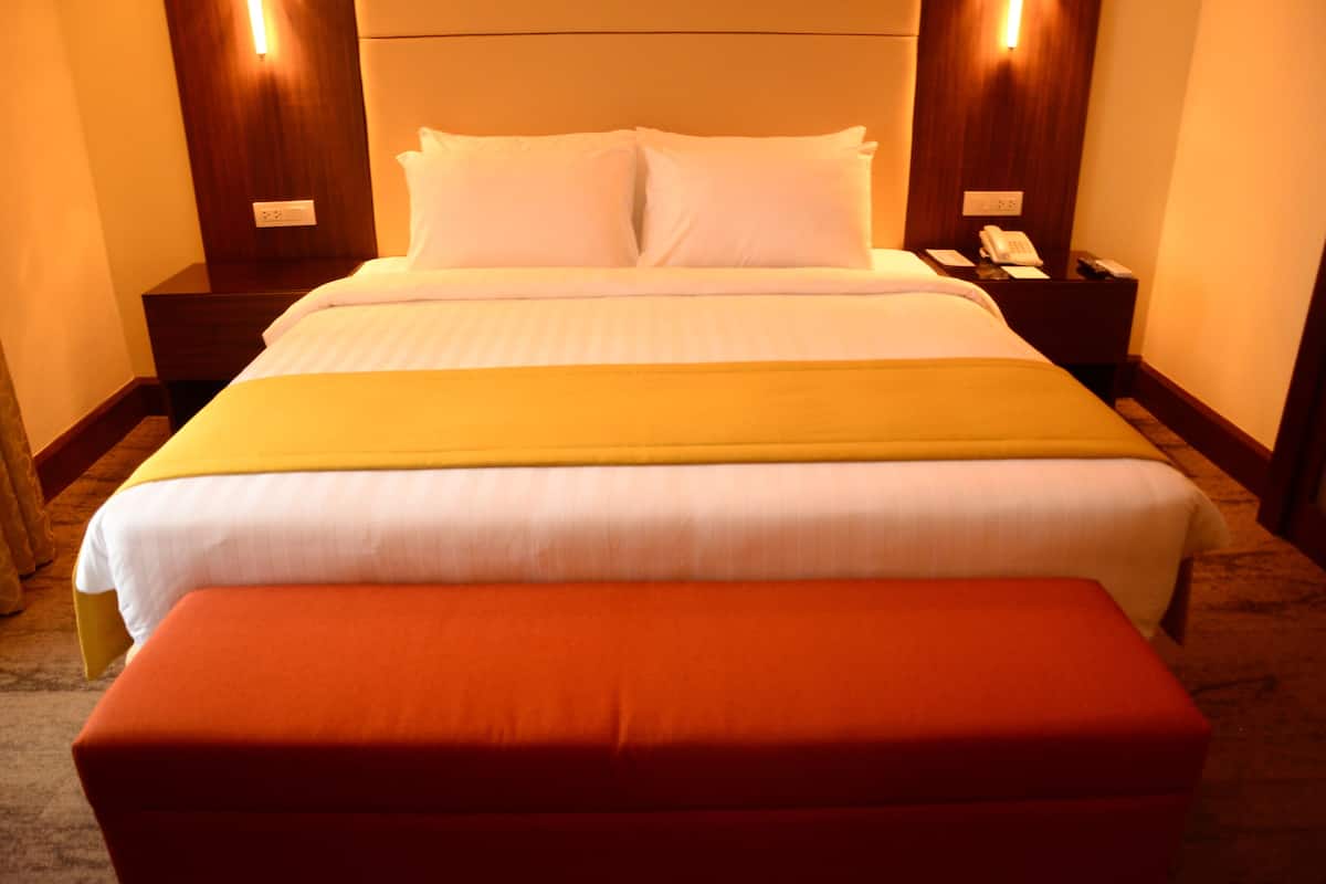 A hotel room with a large bed, a bedside table with a phone, and a red ottoman.
