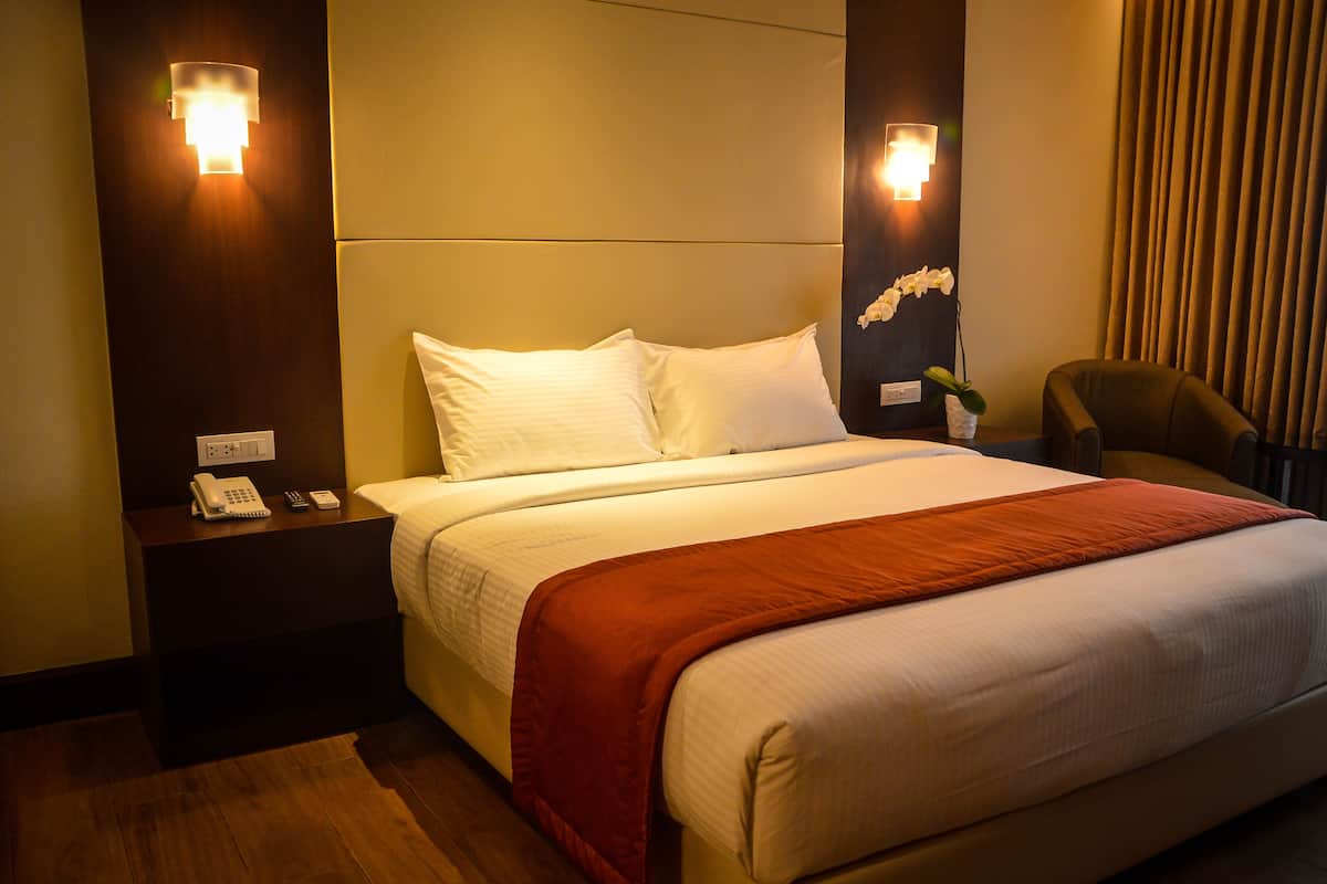 A hotel room with a large bed, a nightstand with a phone, and two wall-mounted lights.