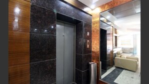 Un ascenseur au design moderne, encadré de murs en marbre foncé et agrémenté d’une poubelle métallique.